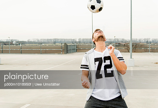 Young man heading soccer ball on parking level