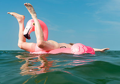 Nude man playing on inflatable flamingo at sea - p429m2019582 by Mischa Keijser