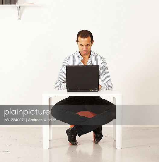 Man using a laptop by a miniature table - Stock Image - Everypixel
