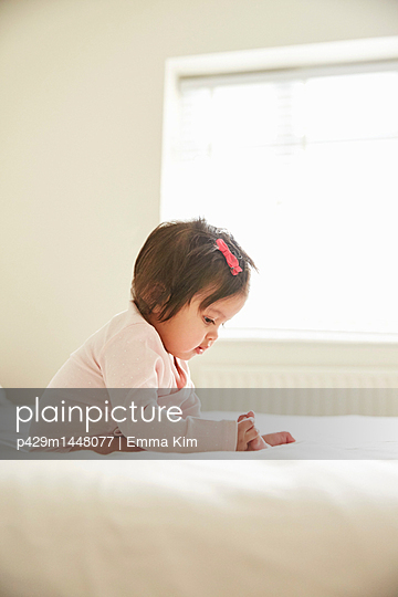 Baby girl sitting up on bed playing with her feet - p429m1448077 by Emma Kim