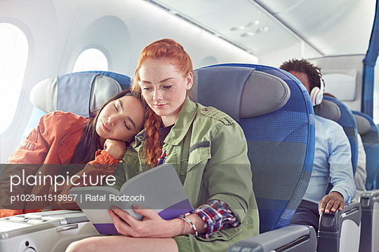 Affectionate young lesbian couple sleeping and reading on airplane - p1023m1519957 by Rafal Rodzoch