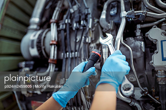 Close-up of hands with tools and jet engine in aircraft maintenance hangar - p924m2459805 by Monty Rakusen