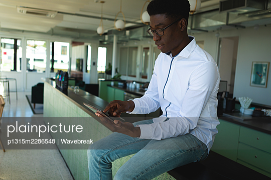 African American man sitting and using a smarphone - p1315m2286548 by Wavebreak